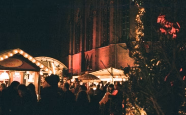 Auf der Adventsführung zu Thema Weihnachten in Alt-Berlin mit Besuch seiner traditionellen Weihnachtsmärkten in der Berliner Altstadt sieht man mehrere romantische Weihnachsmarktstände mit vielen Lichtern im Dunkel und einen Weihnachtsbaum mit der mittelalterlich wirkenden, neogotischen Friedrich Werderschen Kirche im Hintergrund.